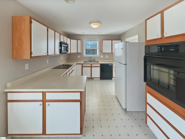 kitchen featuring light floors, a peninsula, a sink, black appliances, and light countertops