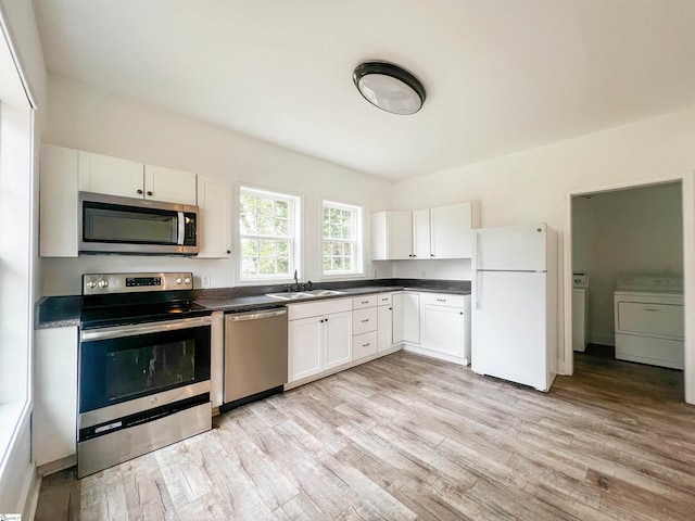 kitchen with dark countertops, stainless steel appliances, independent washer and dryer, white cabinetry, and a sink