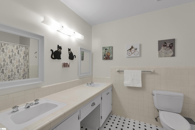 bathroom with a sink, a wainscoted wall, toilet, and tile walls