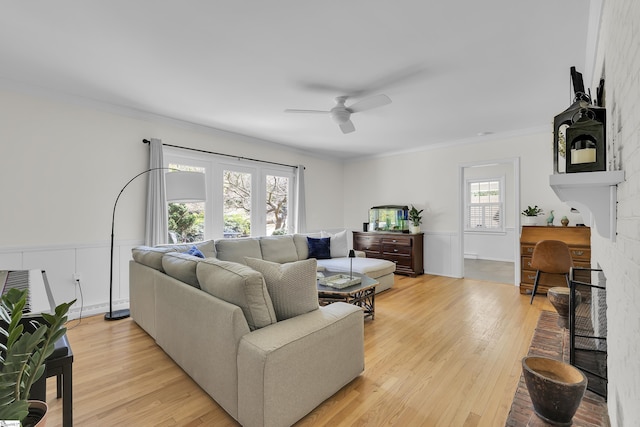 living room with crown molding, light wood-style flooring, a fireplace, and ceiling fan