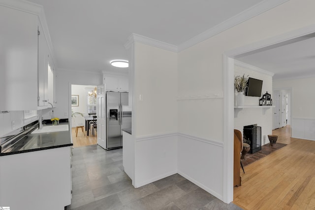 kitchen with a fireplace, ornamental molding, white cabinetry, dark countertops, and stainless steel fridge