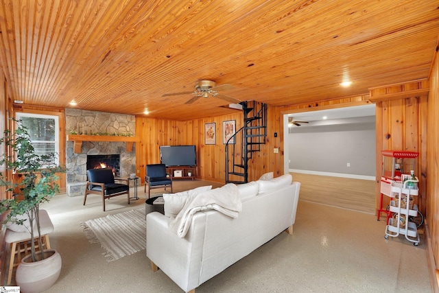 living area with wooden walls, ceiling fan, stairway, a stone fireplace, and wooden ceiling