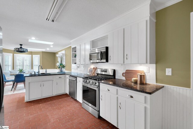 kitchen with wainscoting, appliances with stainless steel finishes, a peninsula, brick floor, and a sink