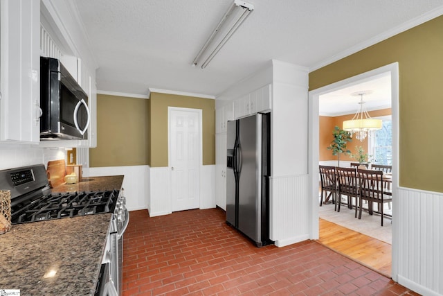 kitchen featuring brick floor, ornamental molding, appliances with stainless steel finishes, wainscoting, and white cabinetry