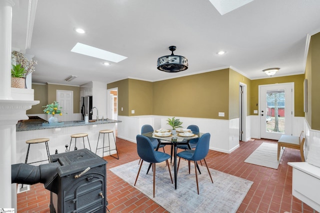 dining space with wainscoting, a skylight, and brick floor