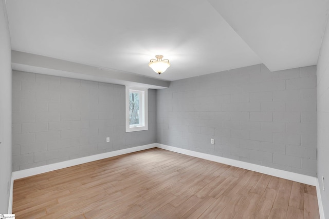 spare room featuring concrete block wall, wood finished floors, and baseboards