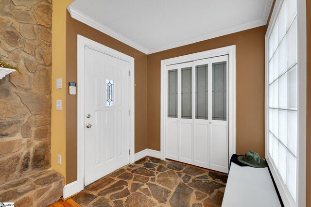 entryway featuring stone finish floor, crown molding, and baseboards