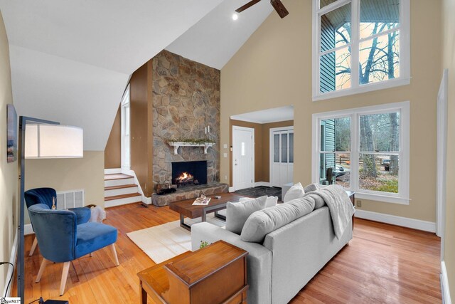 living area featuring baseboards, visible vents, stairs, a stone fireplace, and light wood-type flooring