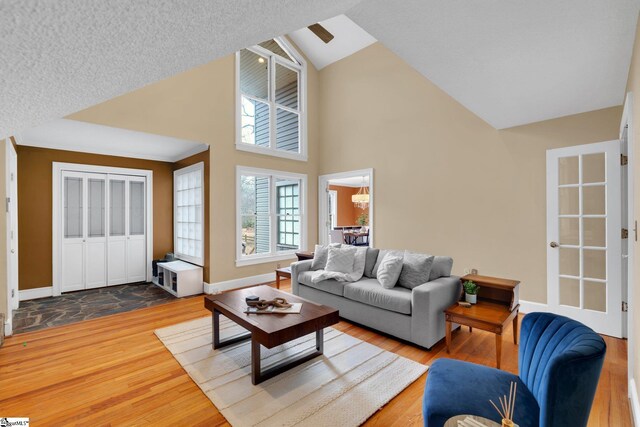 living area with baseboards, high vaulted ceiling, an inviting chandelier, and wood finished floors