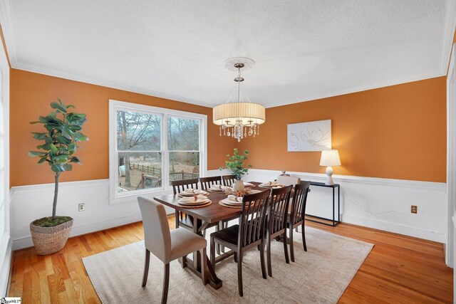 dining space with an inviting chandelier, light wood-style flooring, wainscoting, a textured ceiling, and crown molding