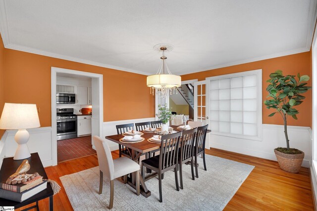 dining area with light wood-type flooring, a wainscoted wall, a chandelier, and crown molding