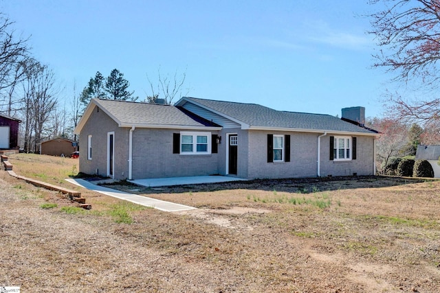 ranch-style house featuring brick siding, a shingled roof, and a patio