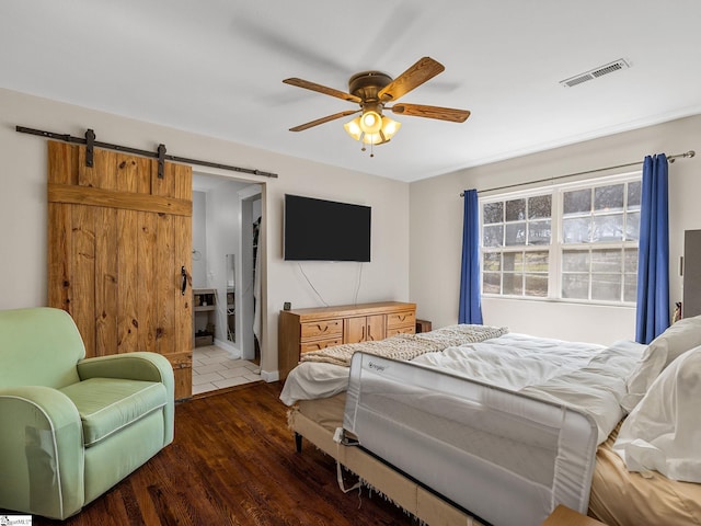 bedroom with visible vents, ensuite bathroom, dark wood-style floors, a barn door, and ceiling fan