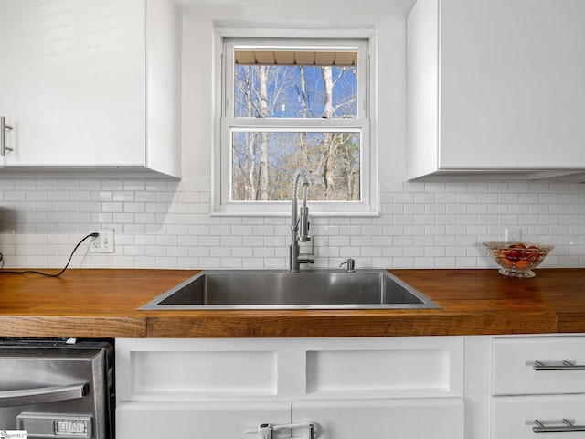 kitchen with tasteful backsplash, white cabinets, wood counters, and a sink