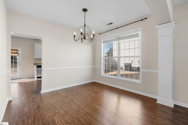 unfurnished dining area featuring visible vents, dark wood finished floors, an inviting chandelier, decorative columns, and baseboards