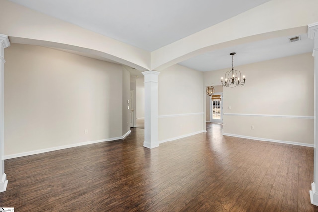 empty room featuring dark wood-style floors, visible vents, baseboards, decorative columns, and arched walkways