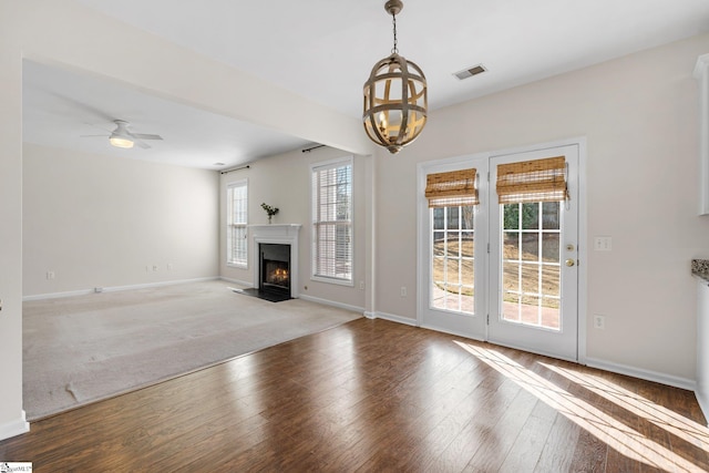 unfurnished living room with visible vents, baseboards, a fireplace with flush hearth, ceiling fan with notable chandelier, and wood finished floors