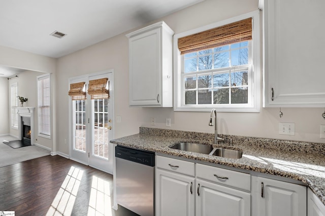 kitchen with dishwasher, wood finished floors, a glass covered fireplace, white cabinetry, and a sink