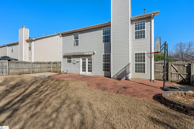 back of house with a gate, a yard, a fenced backyard, a chimney, and a patio area