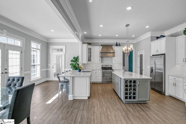 kitchen with wood finished floors, custom range hood, white cabinets, appliances with stainless steel finishes, and a kitchen bar