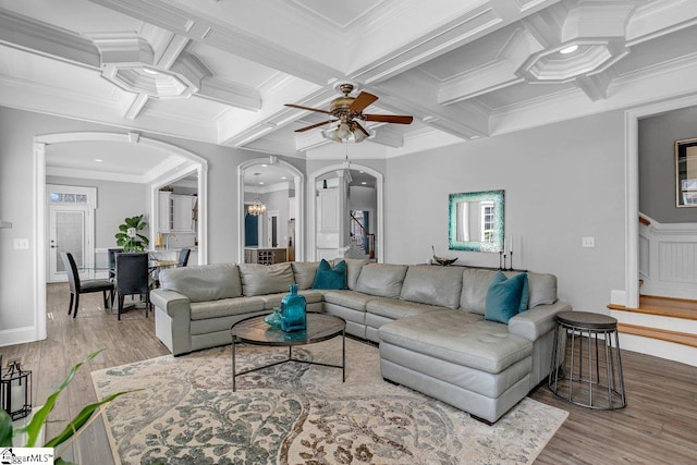 living room with wood finished floors, coffered ceiling, arched walkways, stairs, and crown molding