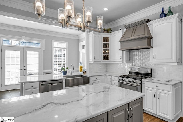 kitchen featuring custom range hood, light stone counters, appliances with stainless steel finishes, white cabinets, and a sink