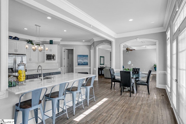 kitchen featuring a kitchen bar, a sink, stainless steel appliances, arched walkways, and white cabinets