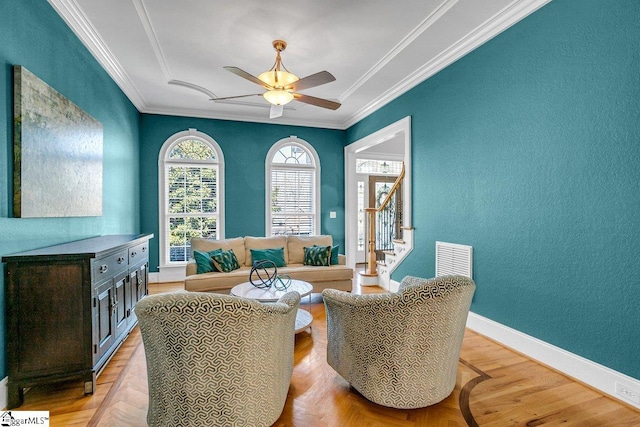 living area with ceiling fan, visible vents, baseboards, and ornamental molding