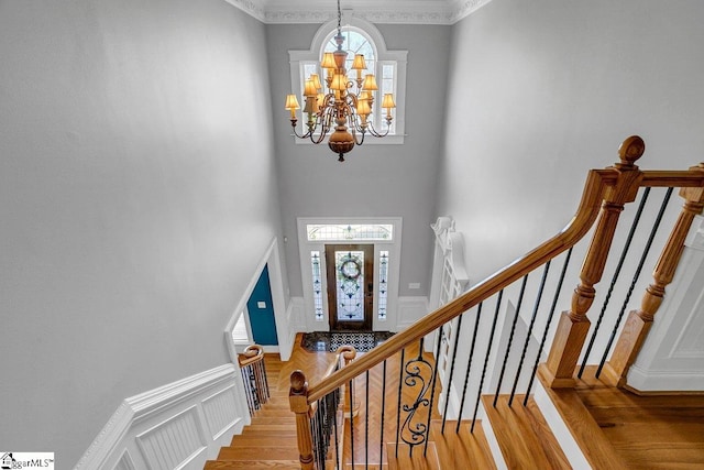 entryway featuring stairway, wood finished floors, an inviting chandelier, wainscoting, and a decorative wall