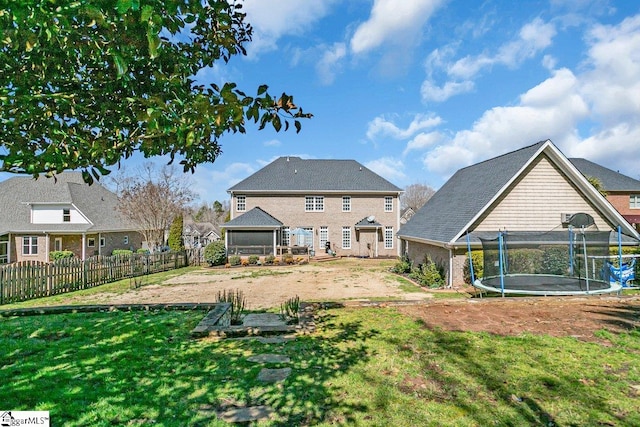 back of house featuring a lawn, a trampoline, and fence