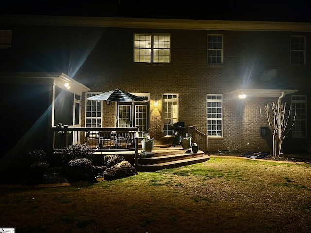 back of house at twilight featuring brick siding, a wooden deck, and a yard