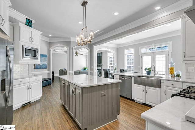 kitchen with a kitchen island, arched walkways, a sink, stainless steel appliances, and white cabinets