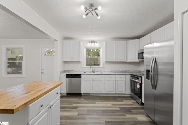 kitchen with a sink, wood counters, stainless steel appliances, white cabinets, and dark wood-style flooring