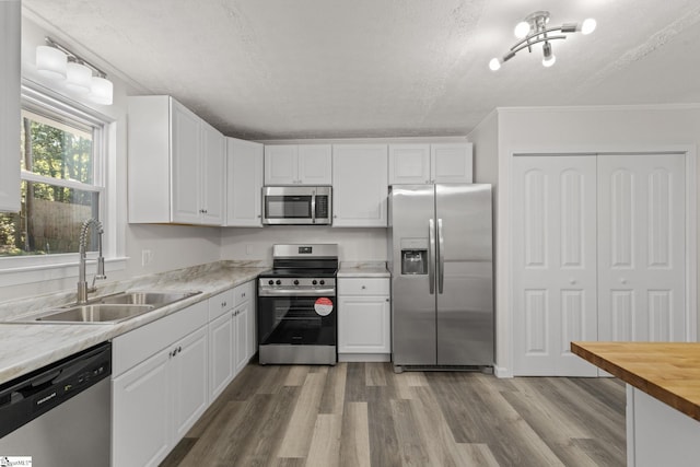 kitchen with wood finished floors, appliances with stainless steel finishes, white cabinetry, and a sink