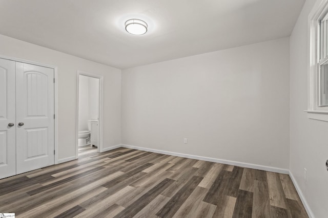 unfurnished bedroom with a closet, baseboards, ensuite bath, and wood finished floors