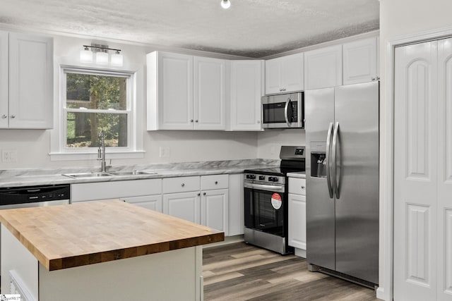 kitchen featuring butcher block countertops, appliances with stainless steel finishes, white cabinetry, and a sink