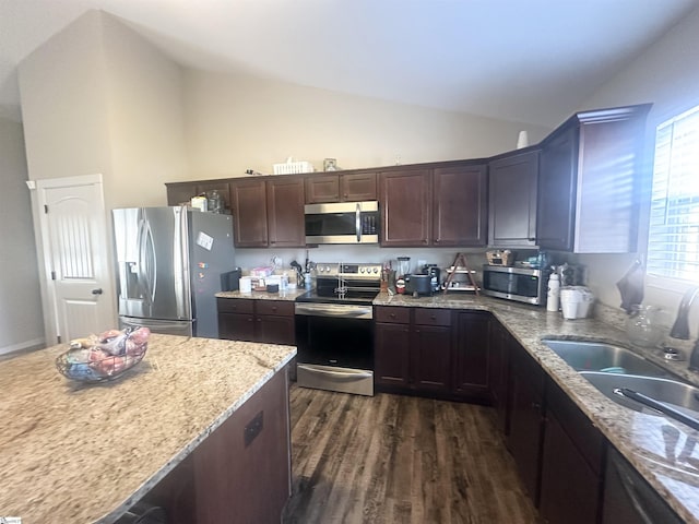 kitchen featuring light stone countertops, dark brown cabinetry, dark wood finished floors, lofted ceiling, and appliances with stainless steel finishes