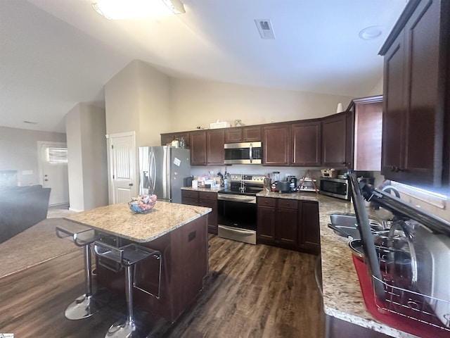 kitchen featuring dark wood-style flooring, dark brown cabinets, appliances with stainless steel finishes, a kitchen breakfast bar, and a center island