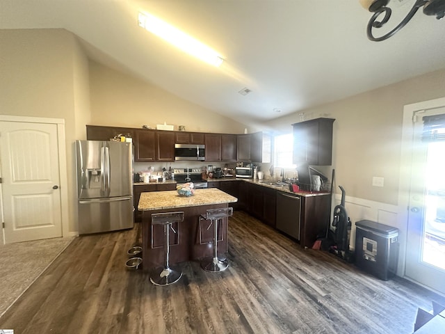 kitchen featuring dark wood-type flooring, vaulted ceiling, appliances with stainless steel finishes, a kitchen bar, and a center island