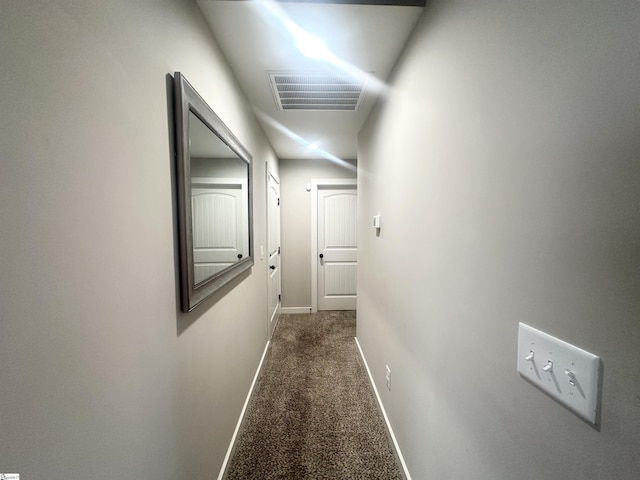 hallway with visible vents, dark carpet, and baseboards