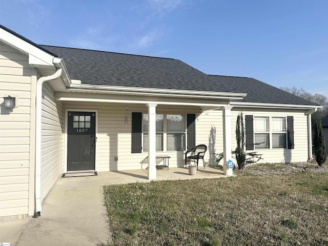 property entrance with a yard, covered porch, and roof with shingles