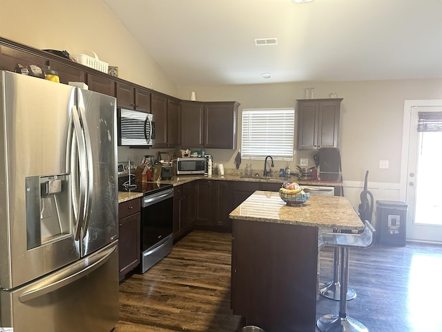 kitchen featuring visible vents, dark brown cabinetry, appliances with stainless steel finishes, a kitchen breakfast bar, and a sink