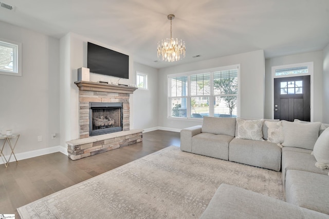 living room featuring visible vents, baseboards, a stone fireplace, and wood finished floors