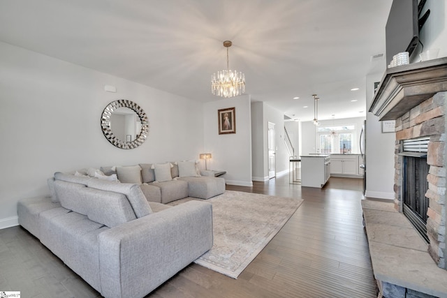 living room with baseboards, a chandelier, dark wood finished floors, a stone fireplace, and recessed lighting