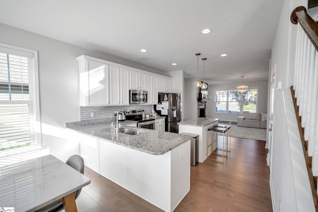 kitchen featuring dark wood-style floors, light stone countertops, stainless steel appliances, decorative backsplash, and a center island