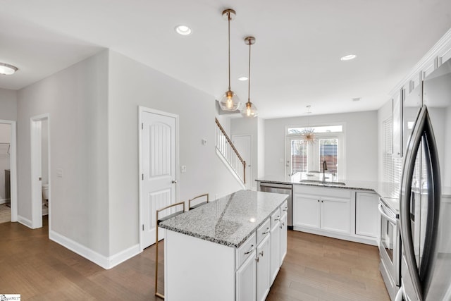 kitchen with a peninsula, stainless steel appliances, wood finished floors, white cabinetry, and a sink