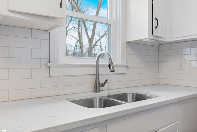 kitchen featuring a sink, light stone counters, tasteful backsplash, and white cabinetry