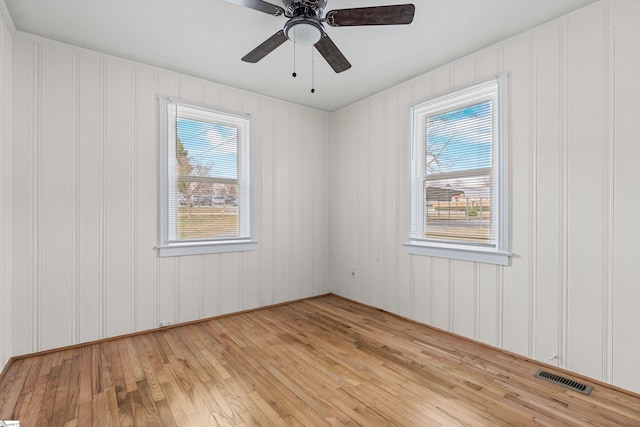 empty room featuring a wealth of natural light, visible vents, light wood-style floors, and a ceiling fan