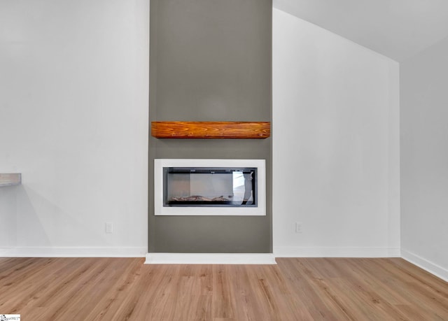 interior details featuring a glass covered fireplace, wood finished floors, and baseboards