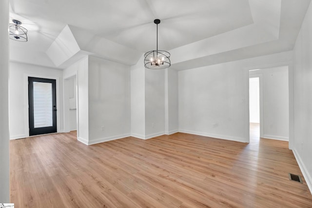 empty room with visible vents, baseboards, a tray ceiling, light wood-style flooring, and an inviting chandelier